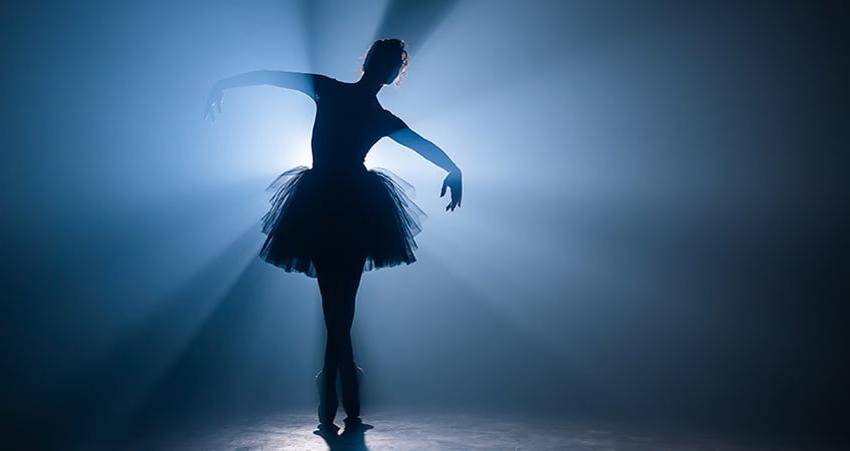 一位芭蕾舞者在灯光昏暗的舞台上摆姿势